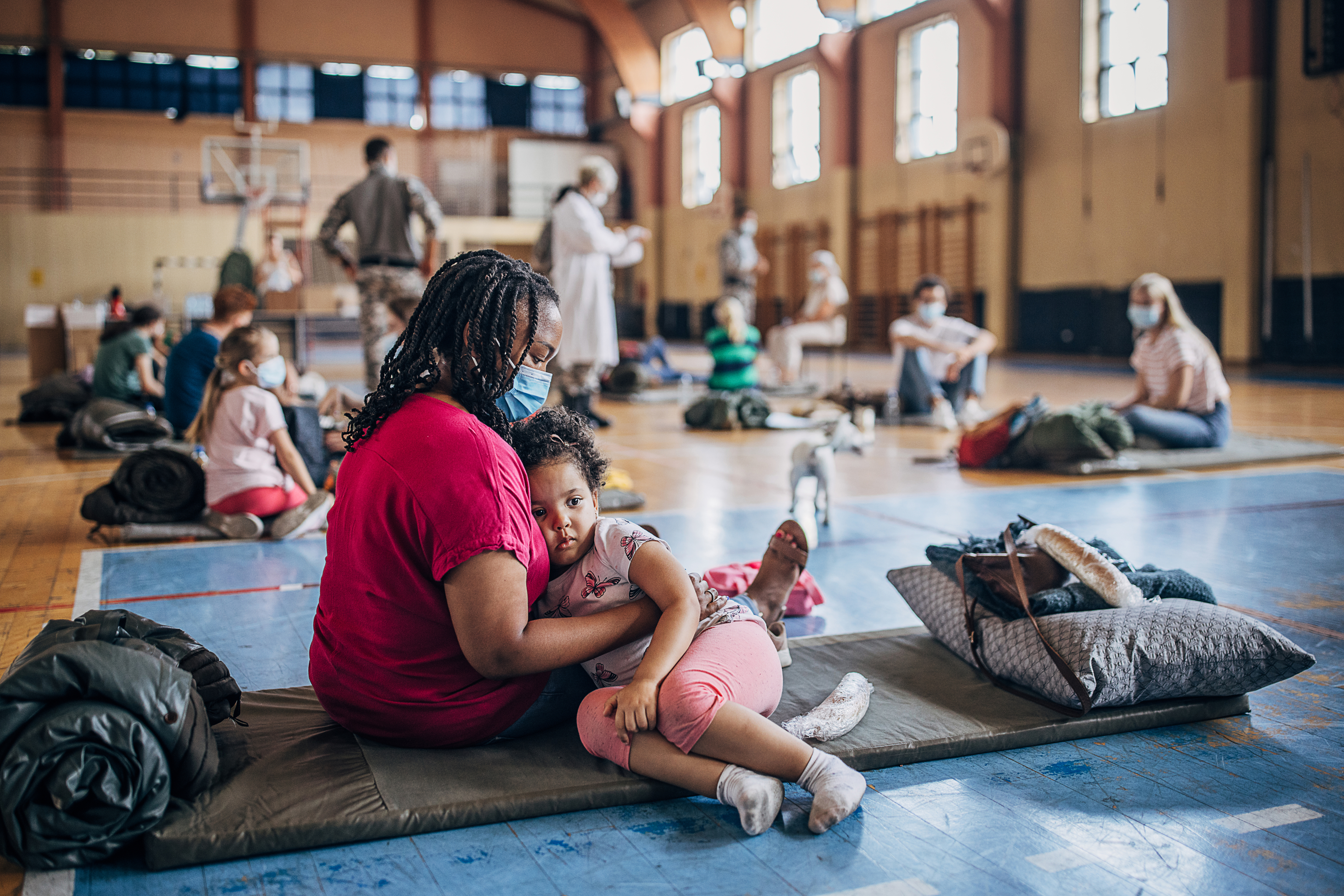 Woman holding child wearing mask sitting on sleeping back in a gym