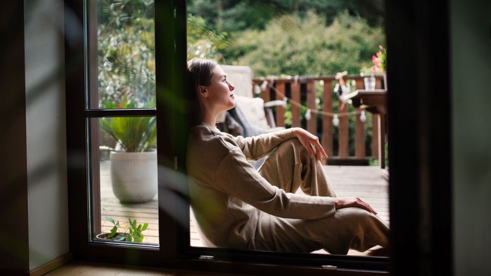 Woman sitting in the sun with a peaceful, calm expression on a back patio 