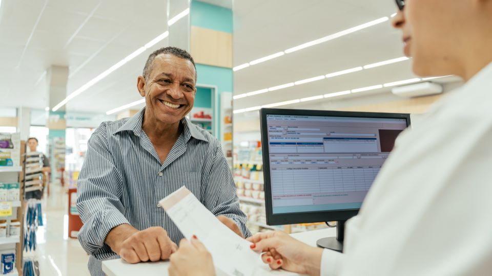 man smiles as he picks up a prescription from a local pharmacy counter