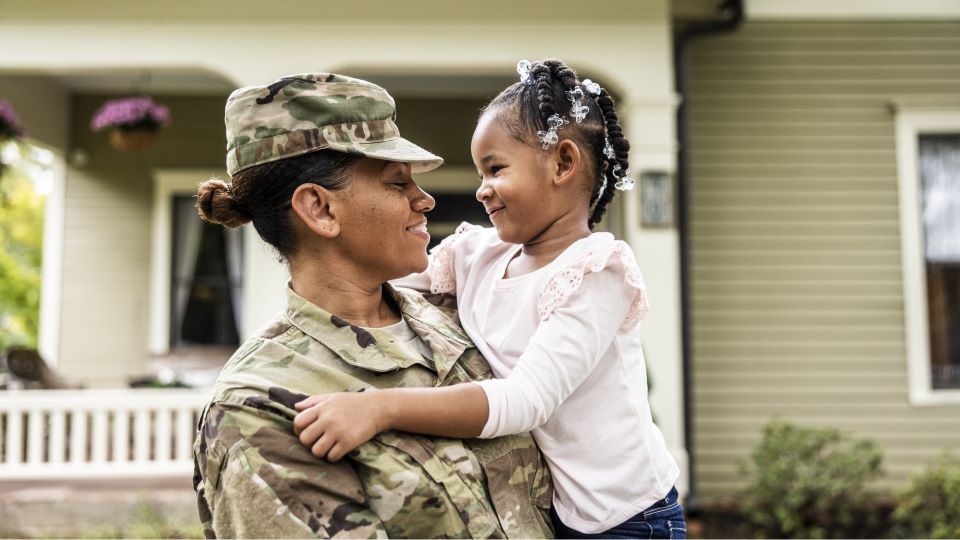 active-duty military woman pictured with her smiling daughter in front of home