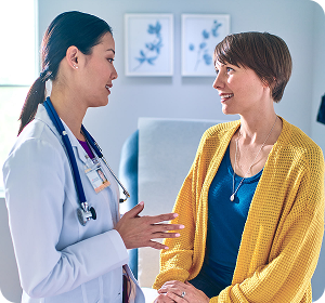 doctor in white coat talking to patient in yellow sweater in exam room
