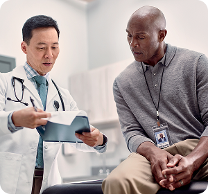 doctor in white coat discussing items on a clipboard with patient sitting in exam room