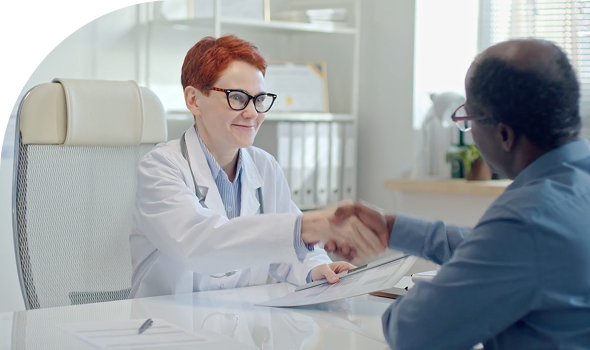 doctor at desk in white coat shaking patient's hand