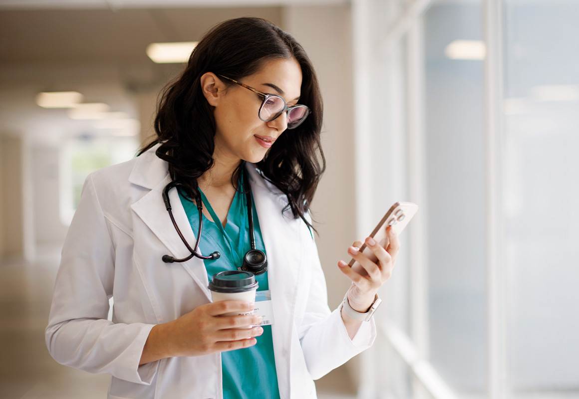 Doctor with glasses holding a coffee and checking their phone
