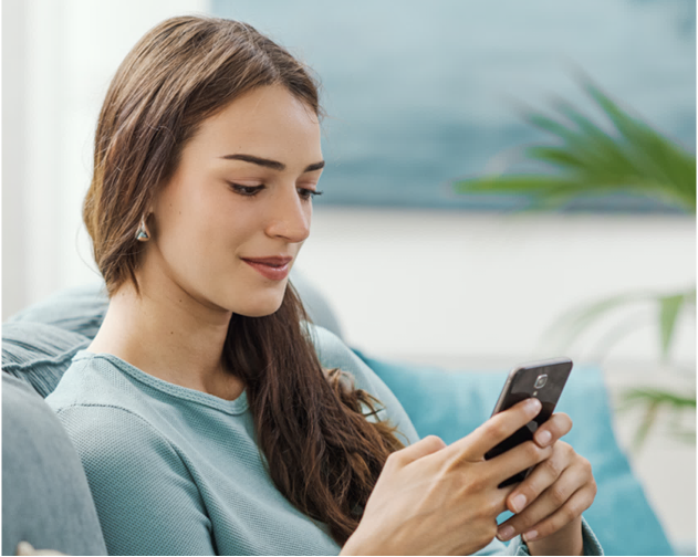 Women in blue shirt sitting on a couch on her cell phone