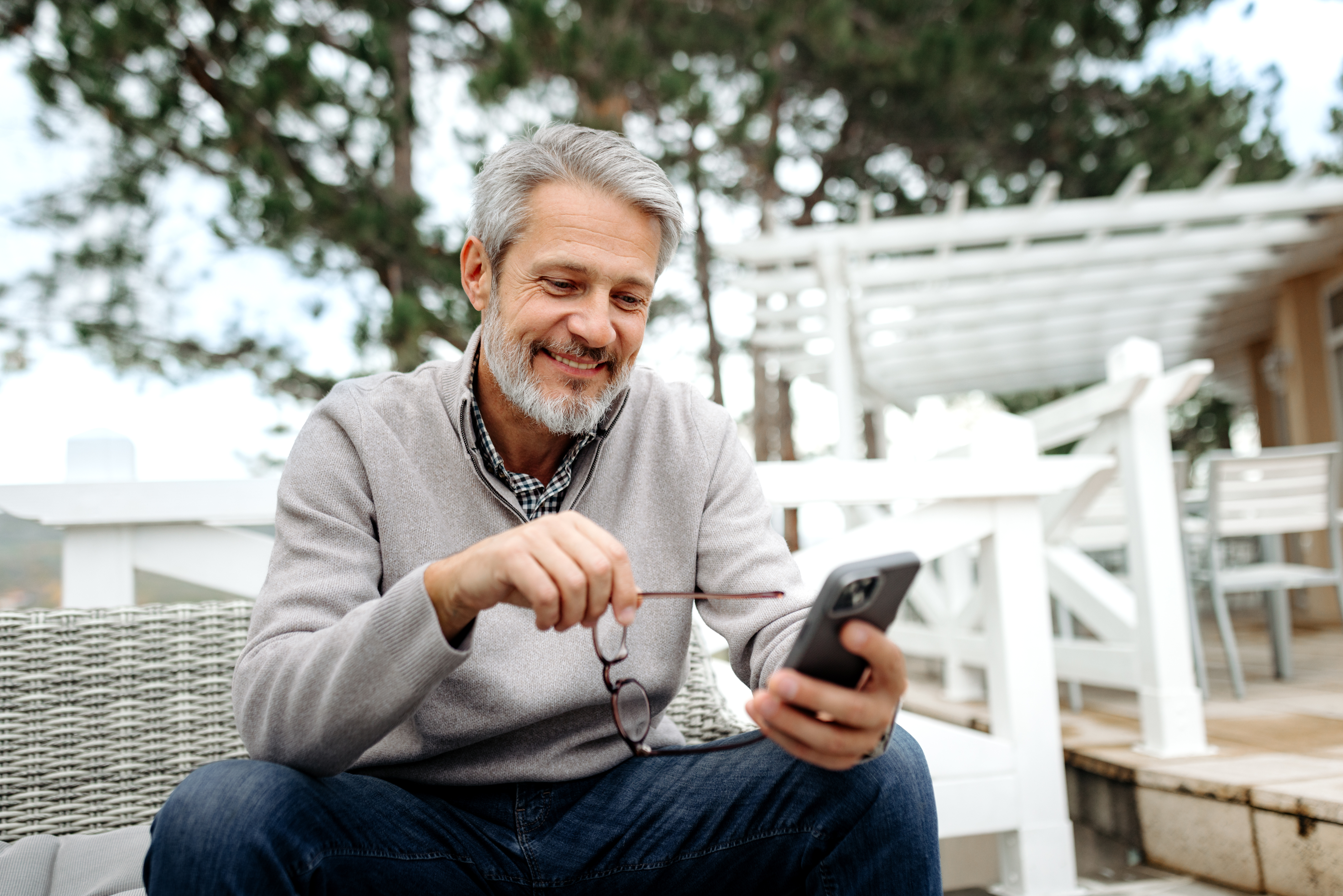 man holding his glasses smiling at his phone
