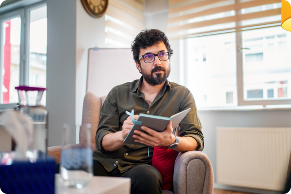 man sitting in a chair in glasses taking notes in a notebook