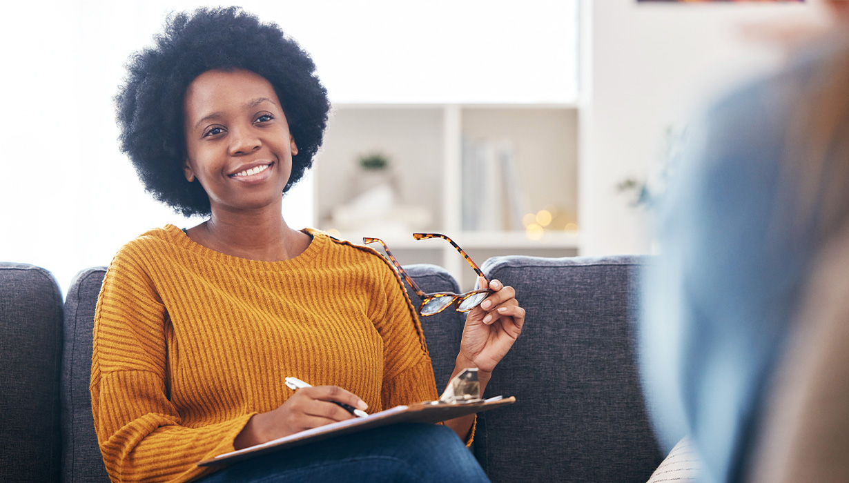 woman holding glasses and smiling while taking notes on a clipboard