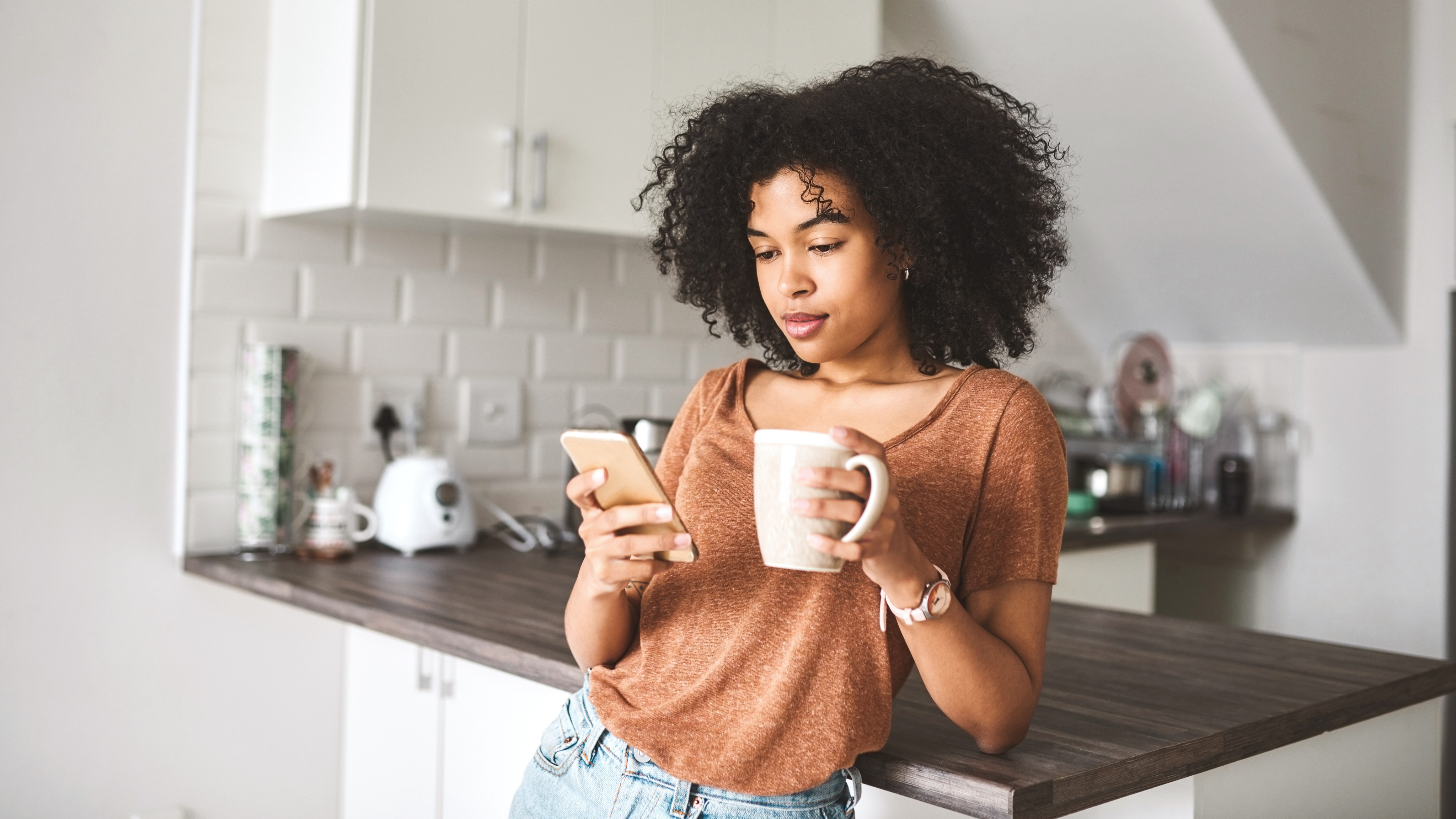 woman holding her cell phone and a coffee mug