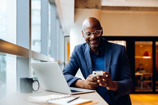 man smiling at phone with laptop on table in front of him