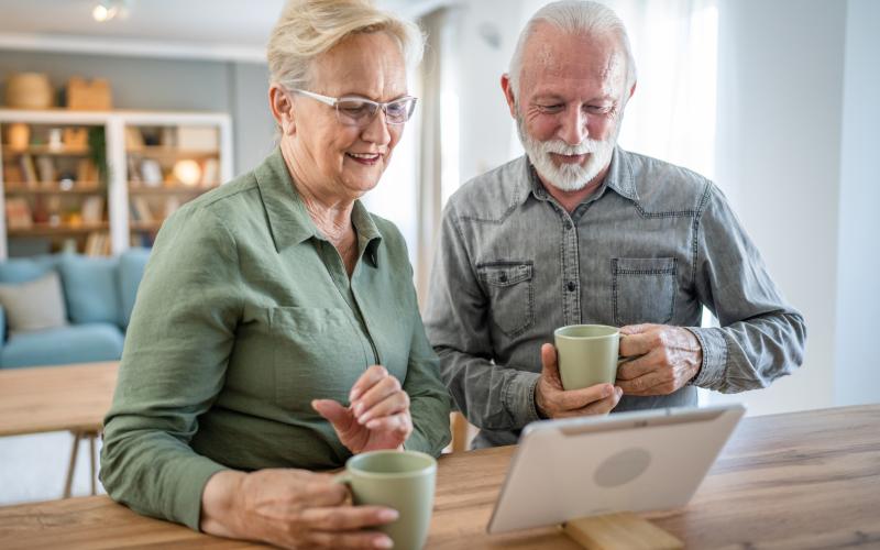 Smiling elder couple look down at tablet