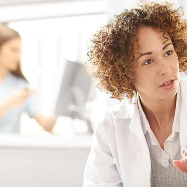 Healthcare professional speaking with patient in bright clinic setting with another staff member in background