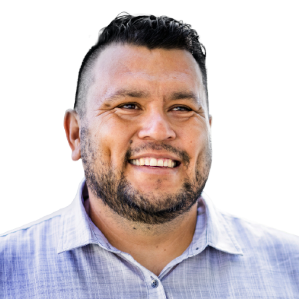 Man with dark hair and beard smiling, wearing a light blue patterned shirt