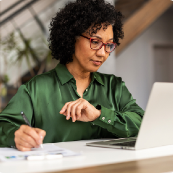 woman in green shirt taking notes while on laptop