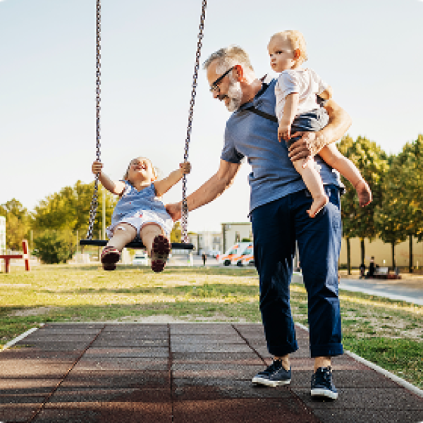 man pushing child on a swing while holding another child