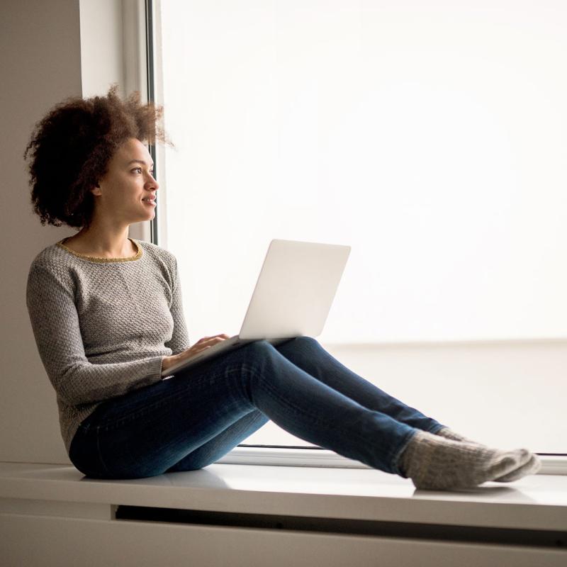 A girl looks out the window on a laptop thinking about her mental health